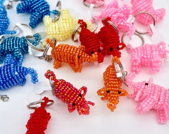 May include: A collection of beaded elephant keychains in various colors, including blue, pink, orange, red, and yellow. The elephants are made of small beads and have a detailed design.