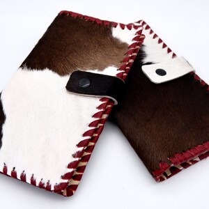 Puede incluir: Dos carteras de piel de vaca marr&oacute;n y blanca con costuras rojas y una correa de cuero negro.