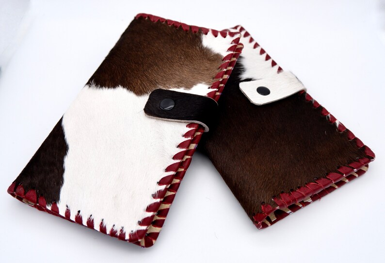 Puede incluir: Dos carteras de piel de vaca marr&oacute;n y blanca con costuras rojas y una correa de cuero negro.