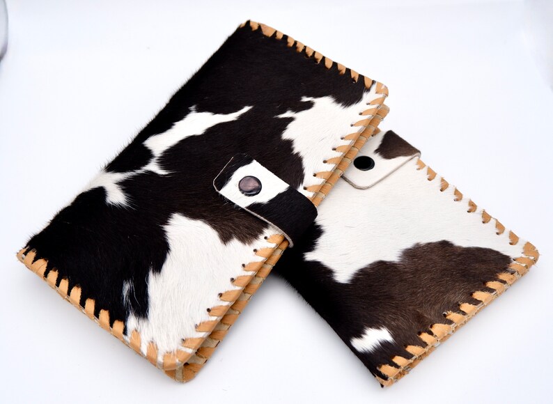 Puede incluir: Dos carteras de piel de vaca en blanco y negro con costuras marrones y una correa de cuero negro en una de las carteras.