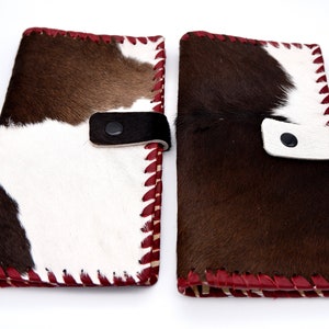 Puede incluir: Dos carteras de piel de vaca marr&oacute;n y blanca con costuras rojas y cierre de correa de cuero negro.