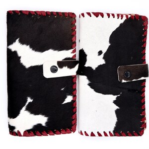 Puede incluir: Dos carteras de piel de vaca negra y blanca con costuras rojas. Las carteras tienen un cierre de solapa con un bot&oacute;n.