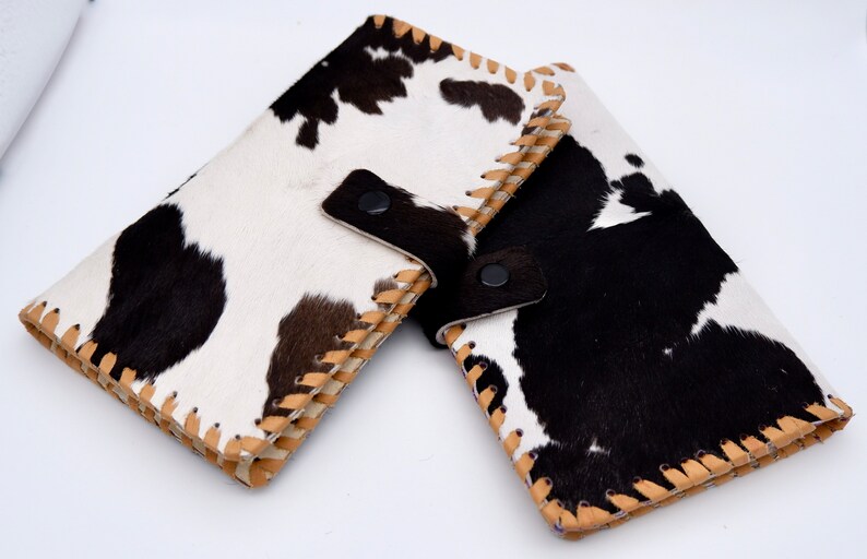 Puede incluir: Dos carteras de piel de vaca en blanco y negro con costuras marrones y un cierre de presi&oacute;n negro.