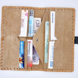Puede incluir: Una cartera de cuero marr&oacute;n con m&uacute;ltiples ranuras para tarjetas y una solapa para efectivo. La cartera est&aacute; abierta y muestra varias tarjetas, incluida una tarjeta de Barclay's, una tarjeta de MoneyGram y una tarjeta de HSC Business Services. Tambi&eacute;n hay varios billetes de libra esterlina dentro de la cartera.