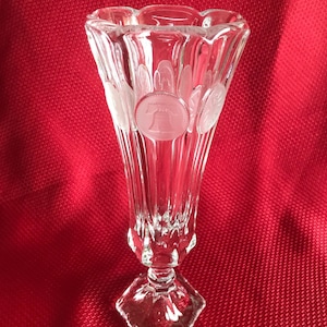 May include: A clear glass vase with a fluted design and a scalloped rim. The vase is decorated with embossed images of the Liberty Bell.