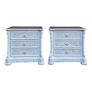 May include: Two matching light blue nightstands with three drawers each. The nightstands have ornate carvings on the drawer fronts and a dark top. The nightstands have a distressed finish and are set against a white background.