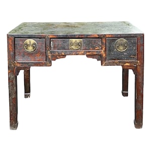 May include: Antique wooden desk with three drawers and brass hardware. The desk has a dark, distressed finish with visible wear and tear. The legs are rectangular and sturdy, and the overall design is reminiscent of Asian furniture.