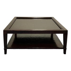May include: A square coffee table with a dark brown, high-gloss finish. The table features a flat top surface with a recessed center panel and a lower shelf for storage. It is supported by four straight, sturdy legs at each corner.