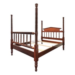 May include: A dark brown wooden four-poster bed frame featuring tall, vertically ribbed posts and a matching headboard with a central arched top rail. The frame includes horizontal side rails and a series of wooden slats for mattress support.