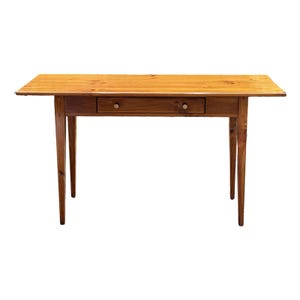 May include: A wooden desk with a natural finish. The desk has a rectangular top, a single drawer with two round knobs, and four tapered legs. The desk is approximately 48 inches long.