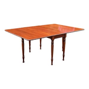 May include: A wooden drop leaf table with a mahogany finish and turned legs. The table has two leaves that can be raised or lowered to adjust the size of the table.