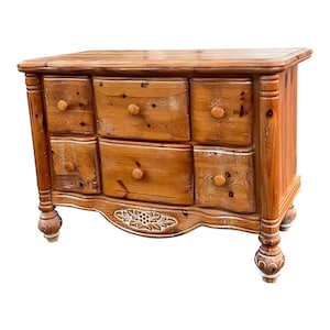 May include: A wooden dresser with six drawers and carved details. The dresser has a light brown finish and is made of pine wood.