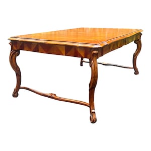 May include: A wooden dining table with a rectangular top and intricate carvings on the legs. The table top has a marquetry design with geometric patterns in shades of brown and beige.