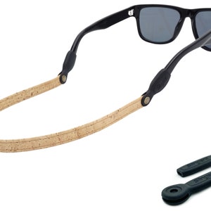 K&ouml;nnte beinhalten: Ein Sonnenbrillenband aus Kork und Leder mit schwarzen Gummieins&auml;tzen. Das Band ist beige mit einem braunen Lederakzent. Die Gummieins&auml;tze haben den Schriftzug "Snapz" aufgedruckt.