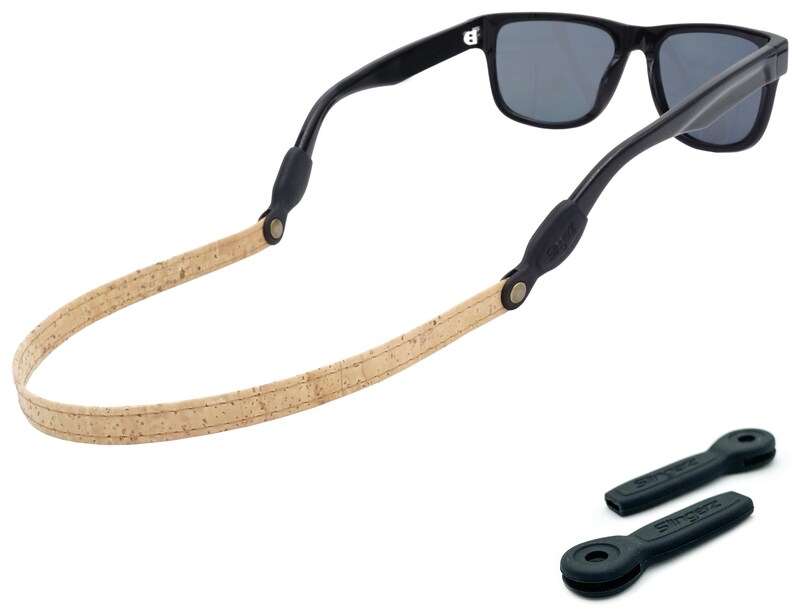 K&ouml;nnte beinhalten: Ein Sonnenbrillenband aus Kork und Leder mit schwarzen Gummieins&auml;tzen. Das Band ist beige mit einem braunen Lederakzent. Die Gummieins&auml;tze haben den Schriftzug "Snapz" aufgedruckt.