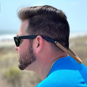 K&ouml;nnte beinhalten: Eine Person tr&auml;gt eine schwarze Sonnenbrille mit einem Kork- und Lederband um den Hals. Das Band ist von der Marke Slingerz.