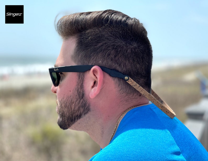 K&ouml;nnte beinhalten: Eine Person tr&auml;gt eine schwarze Sonnenbrille mit einem Kork- und Lederband um den Hals. Das Band ist von der Marke Slingerz.