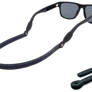K&ouml;nnte beinhalten: Ein dunkelblaues Lederband f&uuml;r Sonnenbrillen mit einem gen&auml;hten Design und schwarzen Gummieins&auml;tzen. Das Band ist an einer schwarzen Sonnenbrille befestigt.