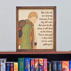 May include: A rectangular wooden framed wall art piece featuring a laser-engraved illustration of a person with a backpack and the text: But in the end, even darkness must pass. A new day will come. And when the Sun shines, it will shine out the clearer. There's some good in this world, and it's worth fighting for.