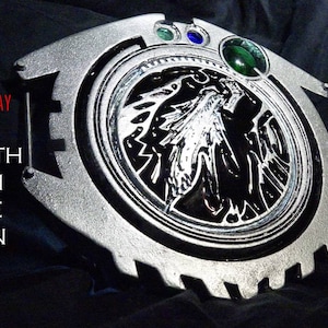 May include: A silver and black metal emblem with a detailed design of a winged figure. The emblem has a green gem in the center and two smaller blue gems on either side. The text "SEPHIROTH EMBLEM REMAKE PATTERN" is visible in the image.