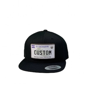 Può includere: Cappello nero e bianco in stile targa personalizzata con il testo "EL SALVADOR" e "CUSTOM" con le parole "Dios, Union, Libertad" sotto.
