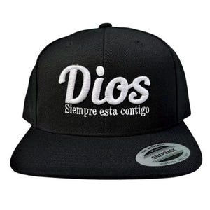 Op de afbeelding: Zwarte baseballpet met witte borduurwerk die "Dios Siempre esta contigo" zegt.