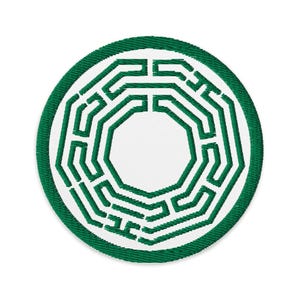 May include: A circular embroidered patch featuring a white background with a dark green stitched maze pattern. The design consists of concentric geometric lines forming a labyrinthine structure, enclosed by a thick, solid dark green border.