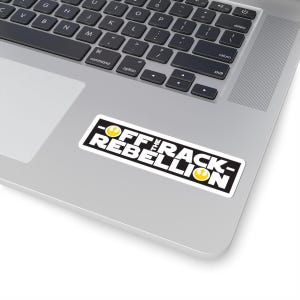 May include: A black and white sticker with the text "Off the Rack - Rebellion" in white letters. The text is surrounded by a black border. The sticker has two yellow Rebel Alliance symbols on either side of the text.