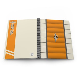 Könnte beinhalten: Ein orangefarbenes und weißes Notizbuch mit einem schwarz-weißen Logo auf dem Cover. Das Logo ist ein Kreis mit einer Linie durch ihn. Das Notizbuch ist auf einer Seite mit einem ähnlichen Design geöffnet. Der Text auf dem Cover lautet "The Sky Above The World".