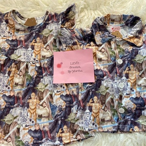 May include: A white and blue Star Wars themed dress and shirt set for children. The fabric features a variety of Star Wars characters, including Darth Vader, Yoda, and C-3PO.
