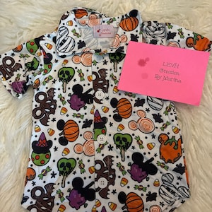 May include: White button-down shirt with a Halloween-themed print featuring Mickey Mouse, pumpkins, candy corn, and other spooky elements. The shirt has a small tag that reads "Levh Creations by Martha".
