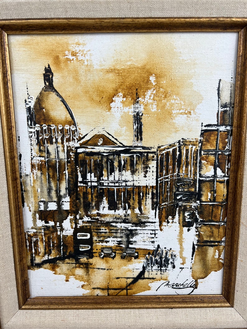 May include: A framed painting of a city scene in brown and white tones. The painting depicts a building with a dome and other buildings in the background. The artist's signature is visible in the bottom right corner.