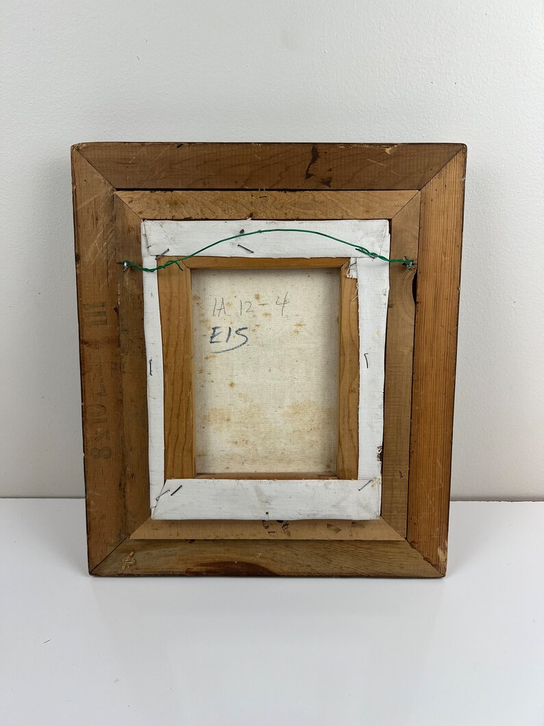 May include: The back of a framed painting with a wooden frame. The canvas is white and has the text "HA 12-44 E15" written on it.