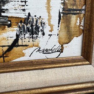 May include: A framed abstract painting with brown, black, and white paint strokes. The painting is signed "Marcella" in the bottom right corner.