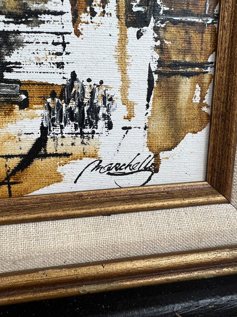 May include: A framed abstract painting with brown, black, and white paint strokes. The painting is signed "Marcella" in the bottom right corner.