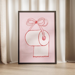Könnte beinhalten: Ein rosa gerahmter Druck eines Toilettenpapier-Rolls mit einer roten Schleife oben. Der Druck ist auf einem rosa Hintergrund.