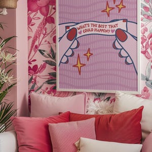 Peut inclure: Une affiche encadr&eacute;e avec le texte "WHAT'S THE BEST THAT COULD HAPPEN?" est affich&eacute;e sur un mur tapiss&eacute; de papier peint floral rose. L'affiche pr&eacute;sente des mains tenant une banni&egrave;re avec le texte et des illustrations d'&eacute;toiles. Plusieurs coussins roses et rouges sont dispos&eacute;s sur un canap&eacute; blanc.
