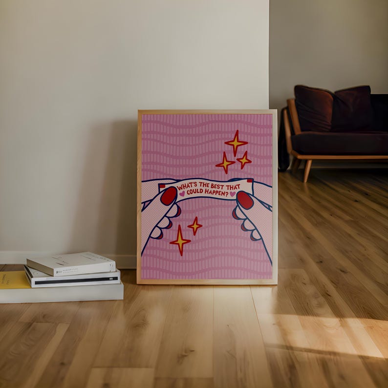 Peut inclure: Une affiche encadr&eacute;e avec un fond rose et un design de biscuit chinois. Le texte dit "WHAT'S THE BEST THAT COULD HAPPEN ?". L'image comprend des mains, des &eacute;toiles et un cadre en bois. L'affiche est pos&eacute;e sur un sol en bois.