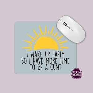 May include: A light blue mouse mat featuring a yellow sun design and the text "I WAKE UP EARLY SO I HAVE MORE TIME TO BE A CUNT." A white wireless mouse is on the mat. The Plum Foolery Gift Company logo is in the bottom right.