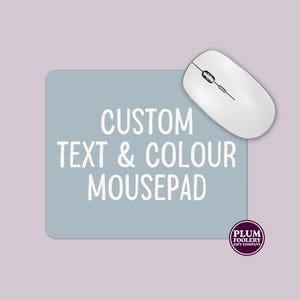 May include: A light blue rectangular mousepad with the text "CUSTOM TEXT & COLOUR MOUSEPAD" in white. A white wireless mouse rests on the mousepad. A circular logo is in the bottom right corner.