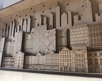 Könnte beinhalten: Ein Holzmodell einer Stadtlandschaft mit verschiedenen Gebäuden, darunter Wolkenkratzer und kleinere Gebäude. Das Modell ist aus lasergeschnittenem Holz gefertigt und hat eine braune Oberfläche.
