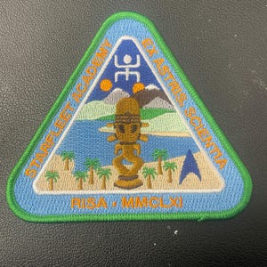 May include: A triangular embroidered patch with a green border featuring a landscape with a blue body of water, palm trees, mountains, and two orange suns. It includes the text STARFLEET ACADEMY, EX ASTRIS, SCIENTIA, RISA, and MMCLXI.