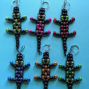 May include: Six beaded lizard keychains with different colored beads. The lizards are black with green, red, pink, blue, orange, and green beads.