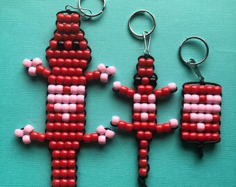May include: Three red and pink beaded lizard keychains of different sizes. The largest lizard is about 6 inches long. The keychains are made with small red and pink beads and have black string for hanging.
