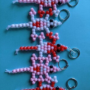 May include: Five beaded lizard keychains in pink, red, and white. Each lizard has a black eye and a silver key ring.