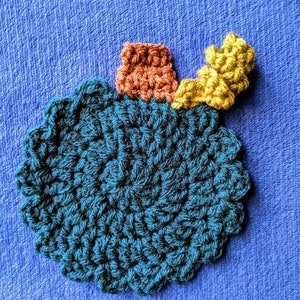 May include: A crocheted teal blue ornament with a brown and yellow crocheted stem.