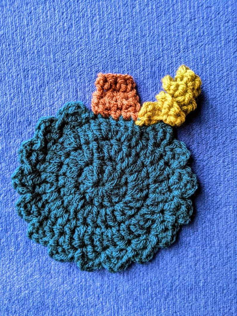 May include: A crocheted teal blue ornament with a brown and yellow crocheted stem.