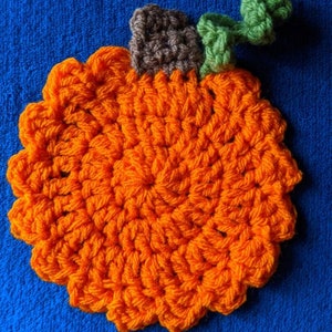 May include: A crocheted orange pumpkin with a brown stem and green leaves. The pumpkin is on a blue background.