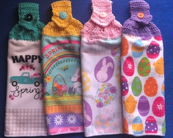 May include: Four crocheted kitchen towels with different spring-themed designs. The first towel features a truck with the words "Happy Spring" and a checkered pattern. The second towel has a rainbow and the words "Spring is a". The third towel has a bunny and the words "Happy Easter". The fourth towel has a pattern of colorful eggs and chicks.