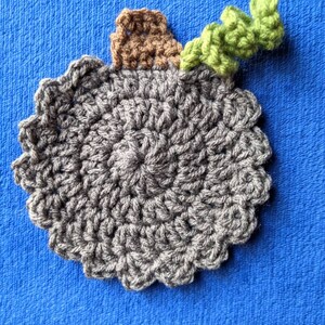 May include: A gray crocheted coaster with a brown crocheted stem and a green crocheted leaf on top.